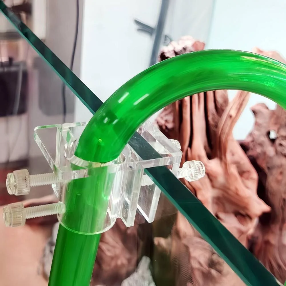 Clear acrylic aquarium pipe holder and hose clamp securing green water tubing to fish tank glass rim